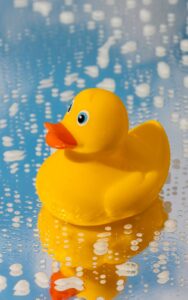Yellow rubber duck on a wet, soapy surface with bubbles around it